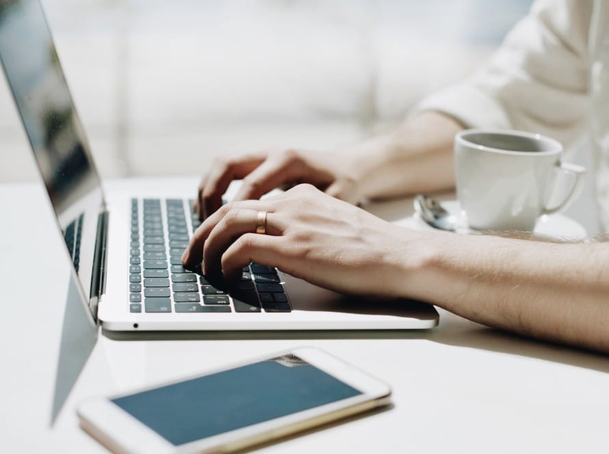 midsection man using laptop by mobile phone coffee cup table scaled